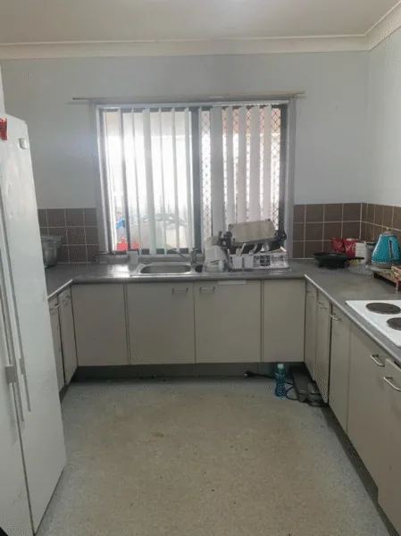 The same kitchen cleaned. The floor is clear, the benches are wiped down and the dishes are away.