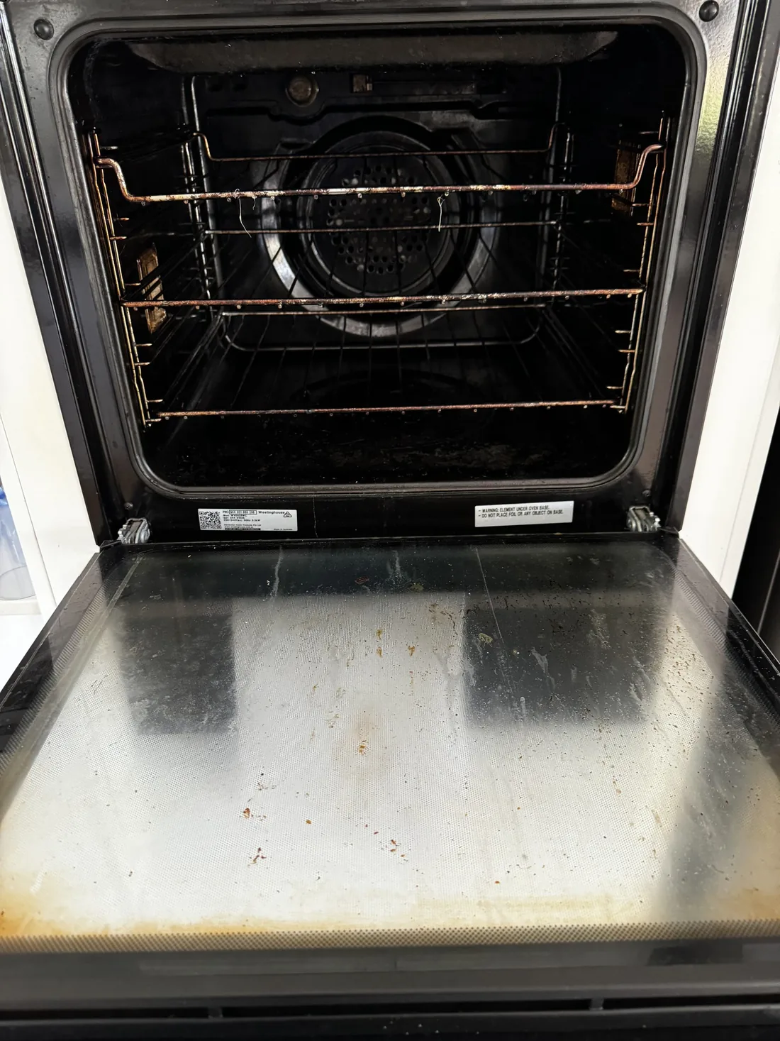 An oven with the door open, showing burnt-on grease across the racks, back plate and door glass.