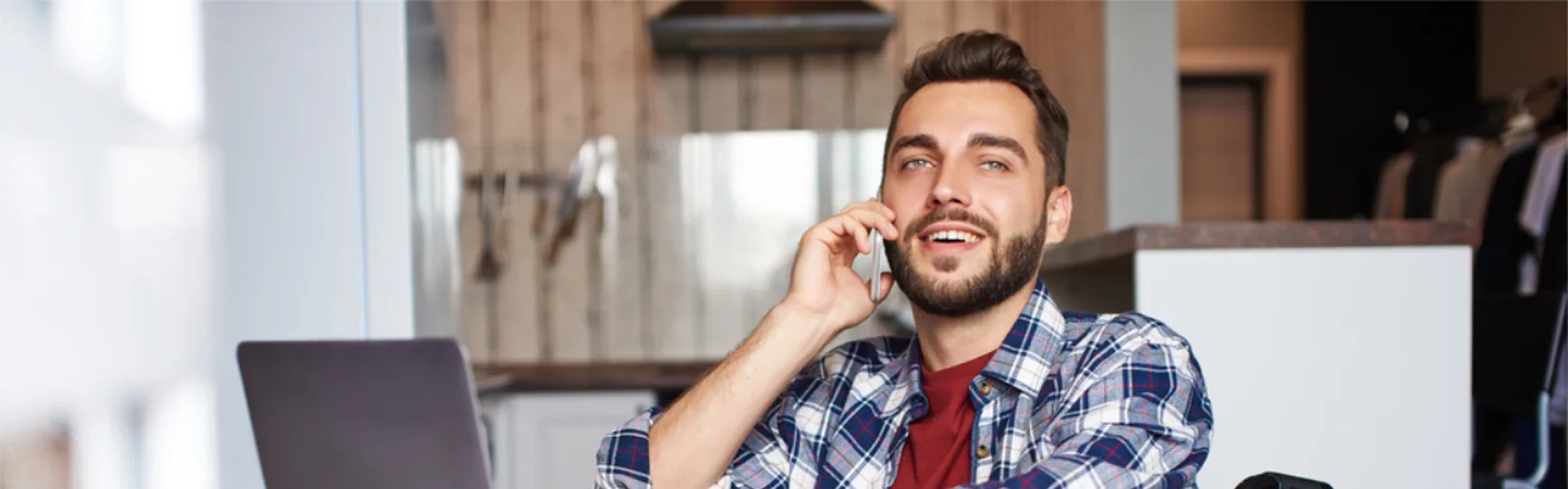 A man smiling while talking on the phone, his laptop open beside him.